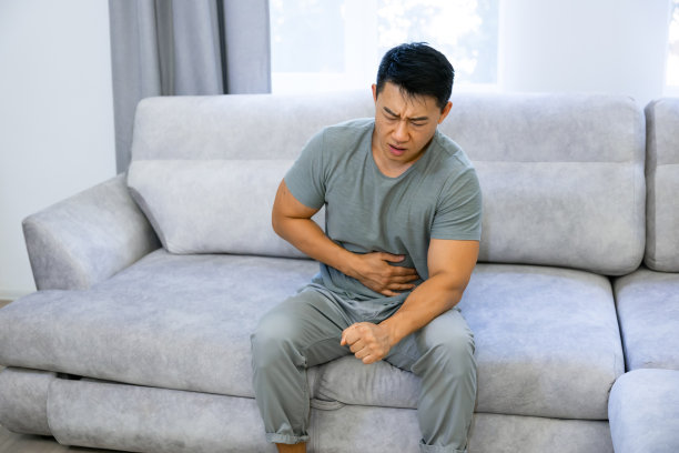 一名男子坐在家里客厅的沙发上，腹痛、腹泻、不适图片下载