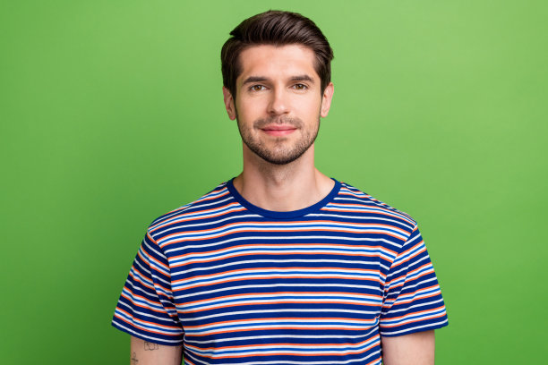 照片中，友好的英俊、冷静、积极的男人留着胡茬，穿着条纹时尚的衬衫，看着相机，孤立在绿色的背景上图片下载