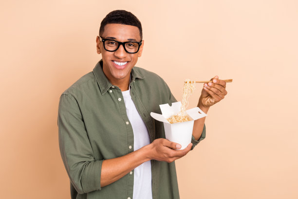 照片中开朗积极的男子穿着卡其布衬衫，戴着眼镜享受着亚洲快餐，空旷的空间孤立的米色背景图片下载