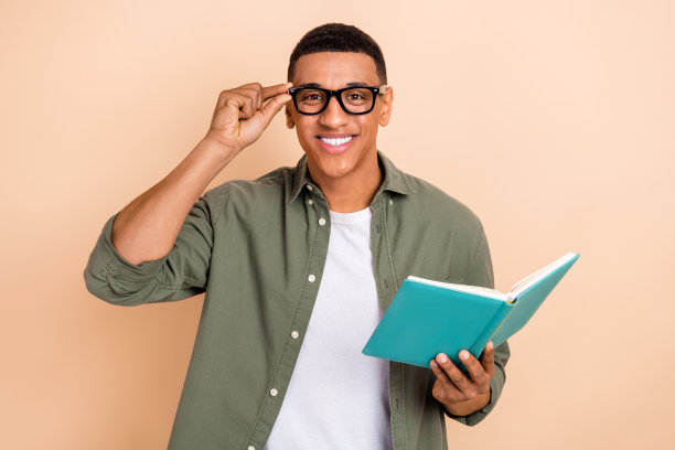 讨人喜欢的英俊聪明的男人的肖像穿着时髦的衬衫触摸眼镜买新书在商店孤立的米色背景图片下载