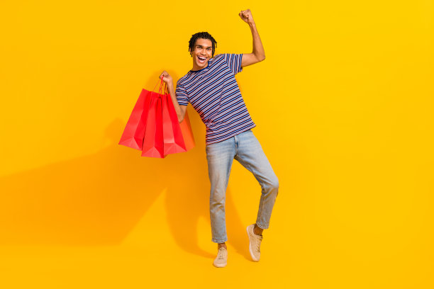 在黄色的背景上，一个兴高采烈的人拿着精品包包举起拳头的全尺寸照片图片下载