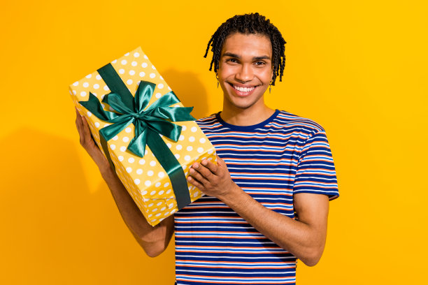 照片中，一个留着脏辫、穿着条纹t恤、双手拿着礼物盒的男人满怀感激、心满意足图片下载