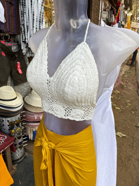 特写图片的塑料人体模型展示奶油色的钩针露脐上衣和一个明亮的黄色包裹圆裙，时尚的沙滩服装在户外市场的服装摊位，重点在前景图片下载
