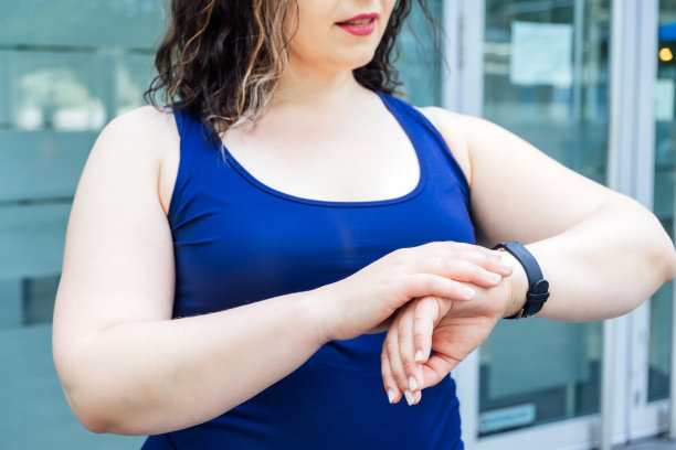 健身可穿戴设备、健身追踪器和智能手表，用于跟踪训练表现。大码健身女人看着手健身追踪器图片下载