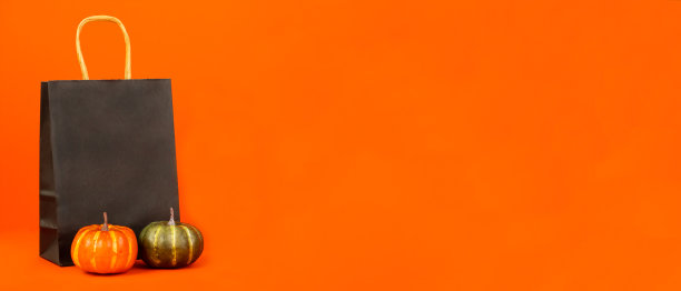 万圣节。黑色纸包装，南瓜站在旁边一个橙色的背景。图片下载