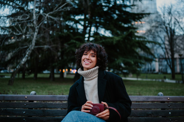 微笑的小女孩坐在公园的长椅上，看着镜头。图片下载