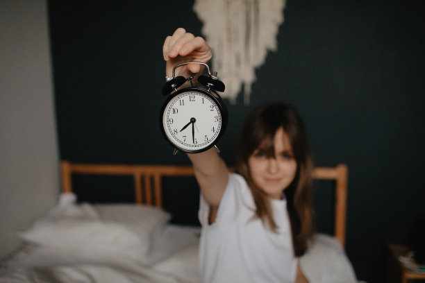 年轻漂亮的女人坐在床上摆弄闹钟图片下载