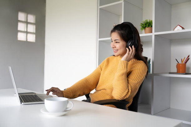 亚洲女性在家里用笔记本电脑，戴着耳机听音乐图片下载