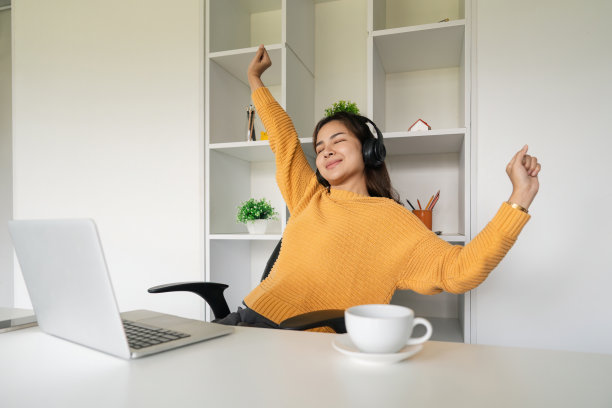 年轻的亚洲快乐女性带着耳机放松伸展，从笔记本电脑的在线学习，视频电话会议，教育，互联网和技术概念中休息图片下载