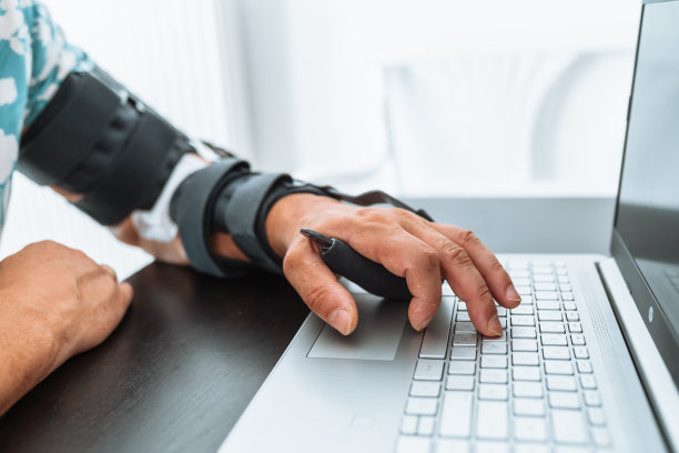 男子可调节关节肘矫形器在笔记本电脑键盘打字图片下载