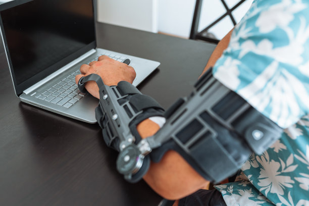 男子可调节关节肘矫形器在笔记本电脑键盘打字图片下载