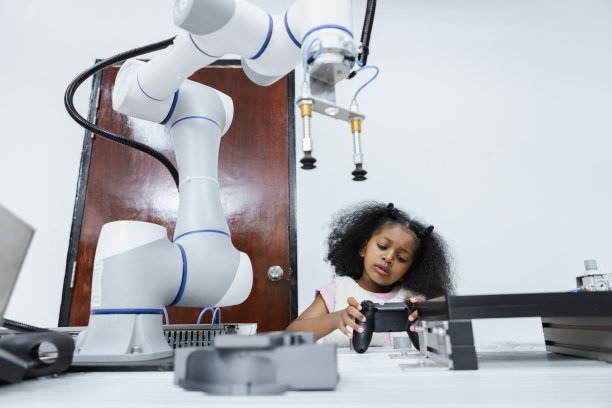 非裔美国女孩使用操纵杆，非裔美国女孩在教室里控制智能机器人手臂。电气系统技能培训。机器人学习创新。STEM教育理念。图片下载
