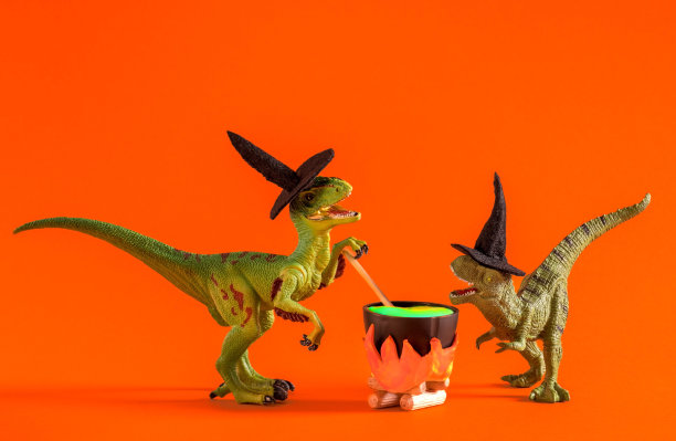 两只戴着女巫帽的搞笑恐龙正在橙色背景的锅里酿造药水。万圣节贺卡。图片下载