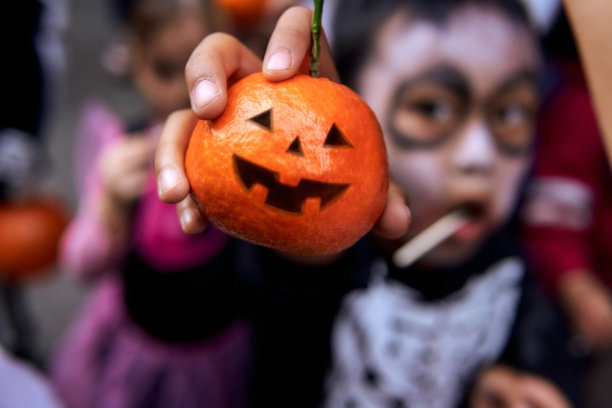 穿着骷髅服装的亚洲孩子展示万圣节橘子南瓜作为健康的食物图片下载
