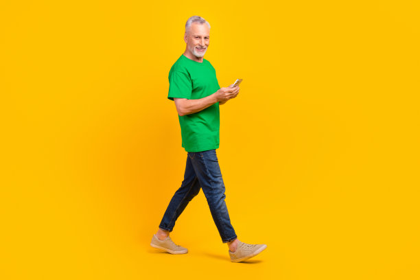 全尺寸的个人资料照片，快乐的老人走路拿着智能手机打字博客文章孤立的黄色背景图片下载