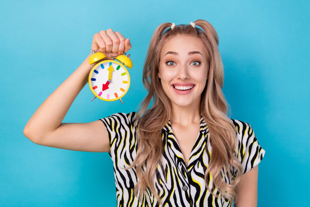 印象深刻的乐观女孩穿着条纹衬衫拿着彩色警报惊讶地盯着孤立的蓝色背景的照片图片下载