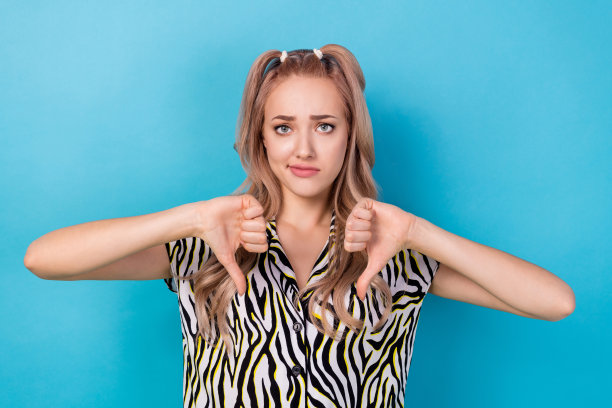 照片不满意的漂亮女孩闷闷不乐的脸，双手手指示范拇指向下孤立在蓝色背景图片下载