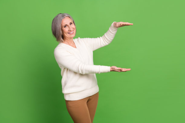 照片的养老金领取者有趣的女人穿白色的背景，灰色的头发测量手拿产品对象孤立的绿色背景图片下载