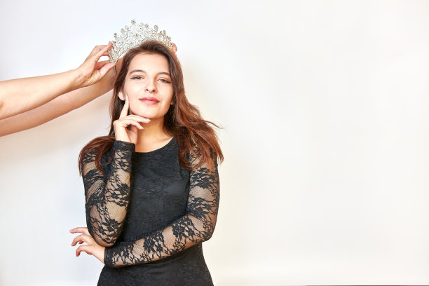 一个穿着黑色连衣裙的漂亮女孩用手捧着一顶皇冠。选美比赛的概念。胜利者的情绪。图片下载