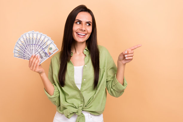 漂亮女人的肖像，长发，穿着绿色的衬衫，拿着钱，看着销售，在米色背景上孤立的空白空间图片下载