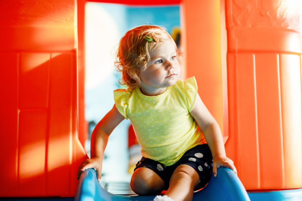 快乐的金发小女孩在日托或托儿所的室内操场上玩得很开心。积极有趣的婴儿孩子微笑。健康的女孩在滑梯上爬。图片下载