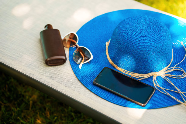 蓝帽子，防晒霜，手机和太阳椅上的太阳镜。图片下载