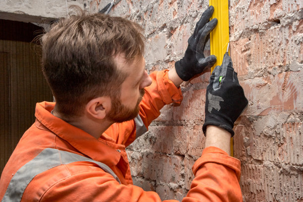 年轻的建筑工人用水平仪在砖墙上画垂直线。图片下载