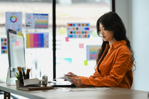 迷人的年轻时尚女子在橙色夹克工作与颜色样品图表在办公室。图片下载