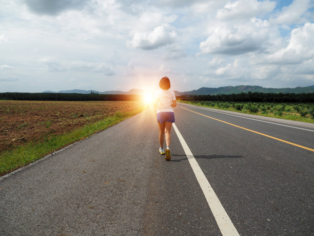 年轻女子在黄昏的灯光下在柏油路上慢跑图片下载