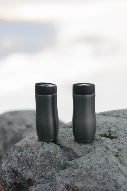 游客保温杯的背景是山，石头和河流，其中的夕阳和云彩的反射。图片下载