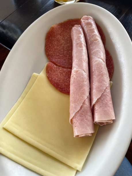 欧陆式早餐的特写图片，餐桌，白色杯子和黑咖啡碟，冷加工肉类和奶酪，不锈钢篮子里装着意大利白面包卷和cornetti(羊角面包)，水果沙拉，重点放在前景图片下载