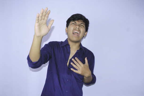 一名亚洲男子在心脏病发作后，双手高举，穿着敞开的海军蓝衬衫，尖叫着捂着胸口图片下载