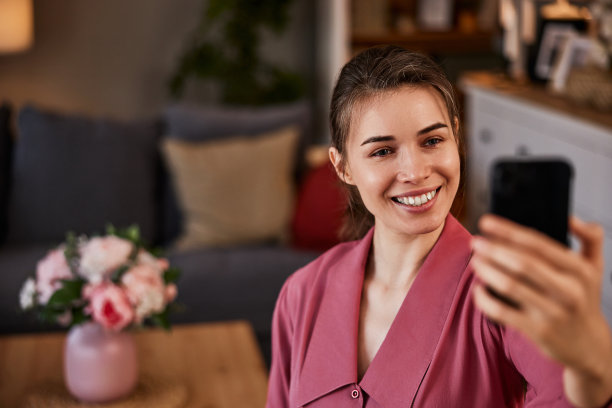 一个微笑的女人在家里用智能手机视频聊天。图片下载