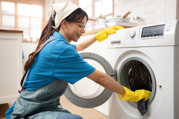 亚洲妇女穿着工作服，女仆在家里打扫卫生，用超细纤维布擦拭厨房的洗衣机图片下载