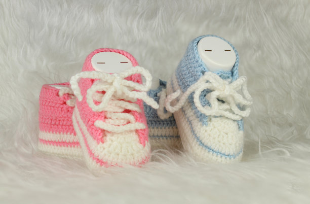 白色毛绒毯子上的粉色和蓝色针织靴。性别党观念观念。婴儿的第一步是给女孩或男孩穿靴子。图片下载