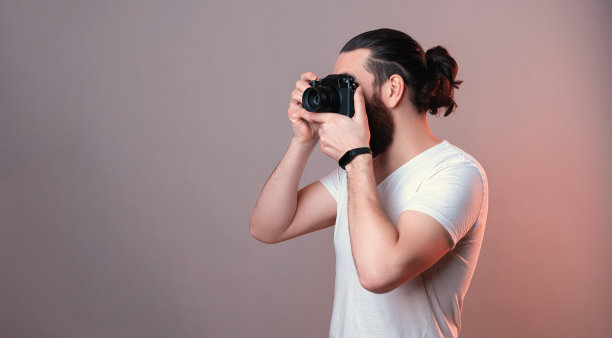 男潮人拿着相机近脸拍照。侧视图。图片下载