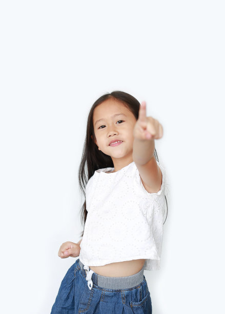 快乐的小女孩的肖像指向和看着相机孤立的白色背景。图片下载