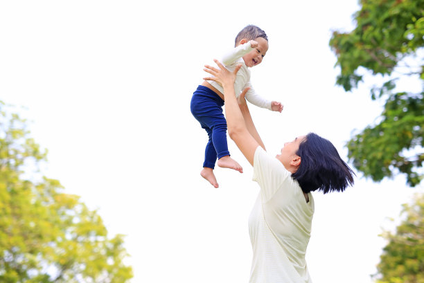 顽皮的亚洲母亲在自然花园里吐出快乐的男婴。母亲在公园里抱着儿子。图片下载