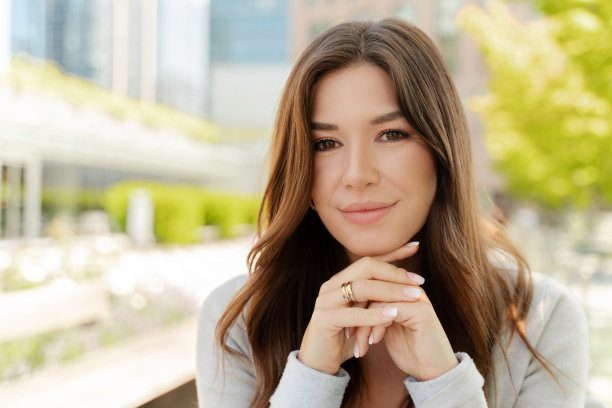 漂亮的头发，迷人的微笑的女人在街上看着相机的肖像图片下载