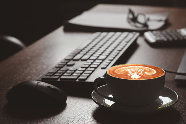 办公室办公桌上一个白色咖啡杯的特写，上面有心形拉花图片下载