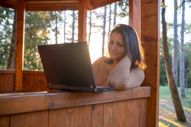夕阳西下，公园里拿着笔记本电脑的开朗年轻女子。图片下载