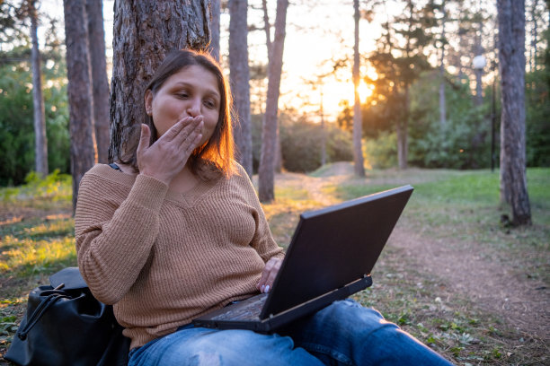 夕阳西下，公园里拿着笔记本电脑的开朗年轻女子。图片下载