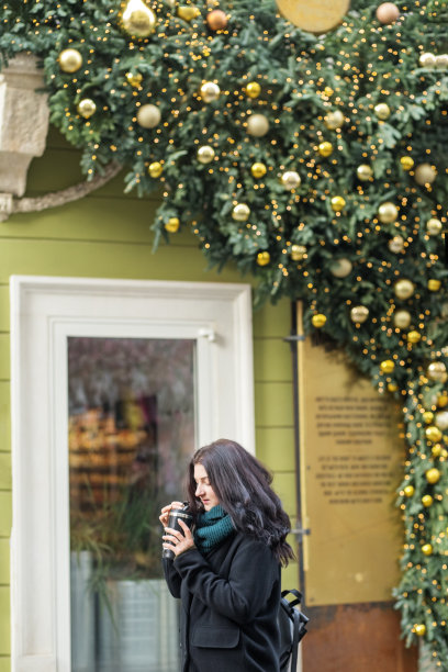 年轻女子在冬天漫步街头时从保温瓶里喝咖啡。圣诞假期图片下载