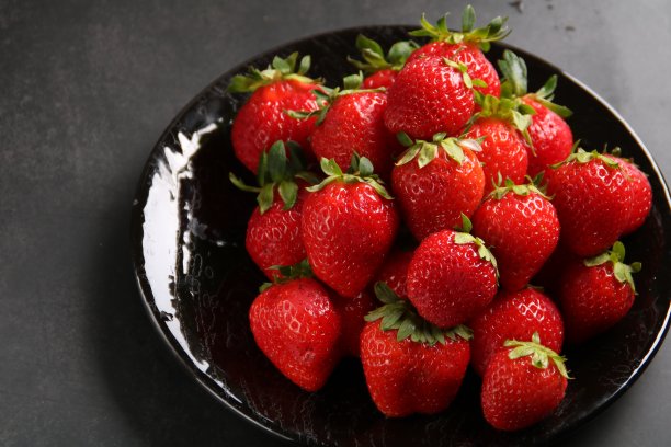 照片甜的甜点，多汁的成熟的红草莓，在黑色的盘子里，在灰色的背景上图片下载