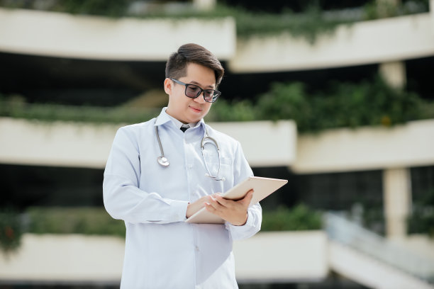 亚洲年轻男性医生穿着实验室大褂，手持听诊器，在医院检查病人的健康结果数据，医务人员，专业的医疗保健服务理念。图片下载