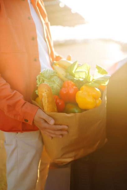 一个穿着时髦衣服微笑着的男人，他的车旁边放着装满健康新鲜食物的购物袋。图片下载