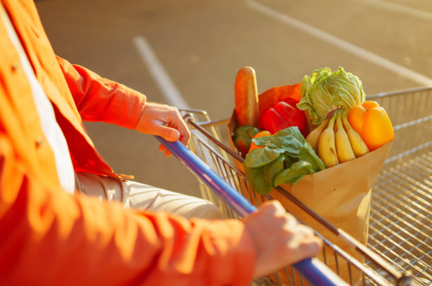 一个穿着时髦衣服微笑着的男人，他的车旁边放着装满健康新鲜食物的购物袋。图片下载