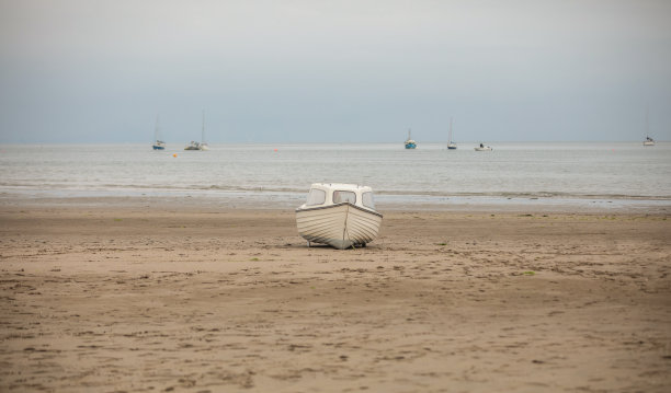 孤立的白色小船被困在沙滩上，等待着另一次涨潮浮出水面。图片下载