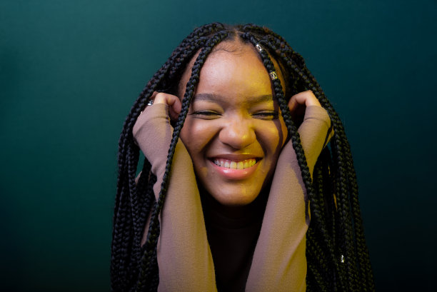 一个扎着小辫，双手放在下巴上微笑的年轻女子的肖像。图片下载