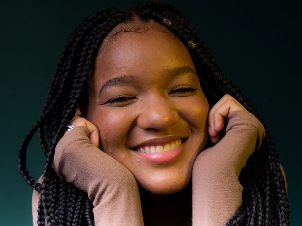 一个扎着小辫，双手放在下巴上微笑的年轻女子的肖像。图片下载